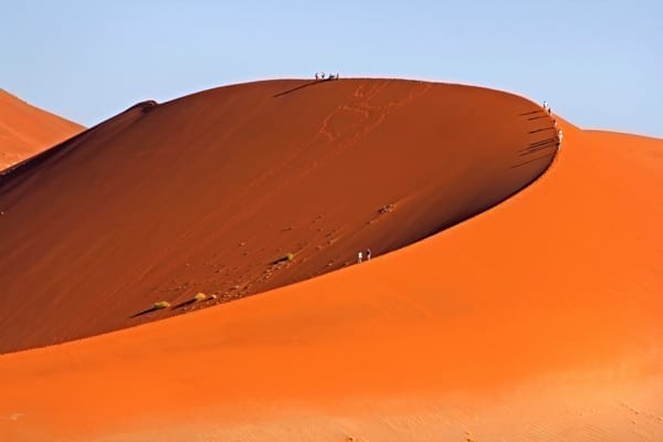 En jättelik, röd sanddyn med pyttesmå människor som klättrar uppför den. Namibia är en bra destination för en safari i Afrika