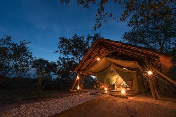 Ett tält är upplyst med oljelampor, runtomkring är det mörkt. Lyxa till semestern med att bo på till exempel Kwambili Safari Lodge, som har prisvärda safaritält och safari i världsklass
