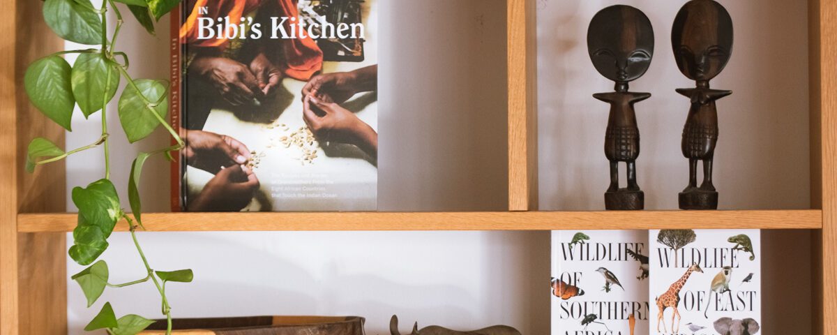 boken "In Bibi's Kitchen" och böckerna "Wildlife of Southern Africa" samt "Wildlife of Eastern Africa" är några av vinsterna på Afrikakompaniets mingel. Här syns böckerna i en bokhylla av trä, omgivna av växter och afrikanska statyer.