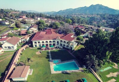 Översiktsvy över Mountain Inn i Eswatini, med en pool i förgrunden och en större hotellbyggnad bakom, och kullar som kuliss.