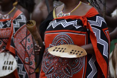 Dansaare i Mantenga Cultural Village i Eswatini. Du ser en färgglatt klädd kvinna med en sköld i handen, det är rörelse runtomkring så man förstår att de dansar.