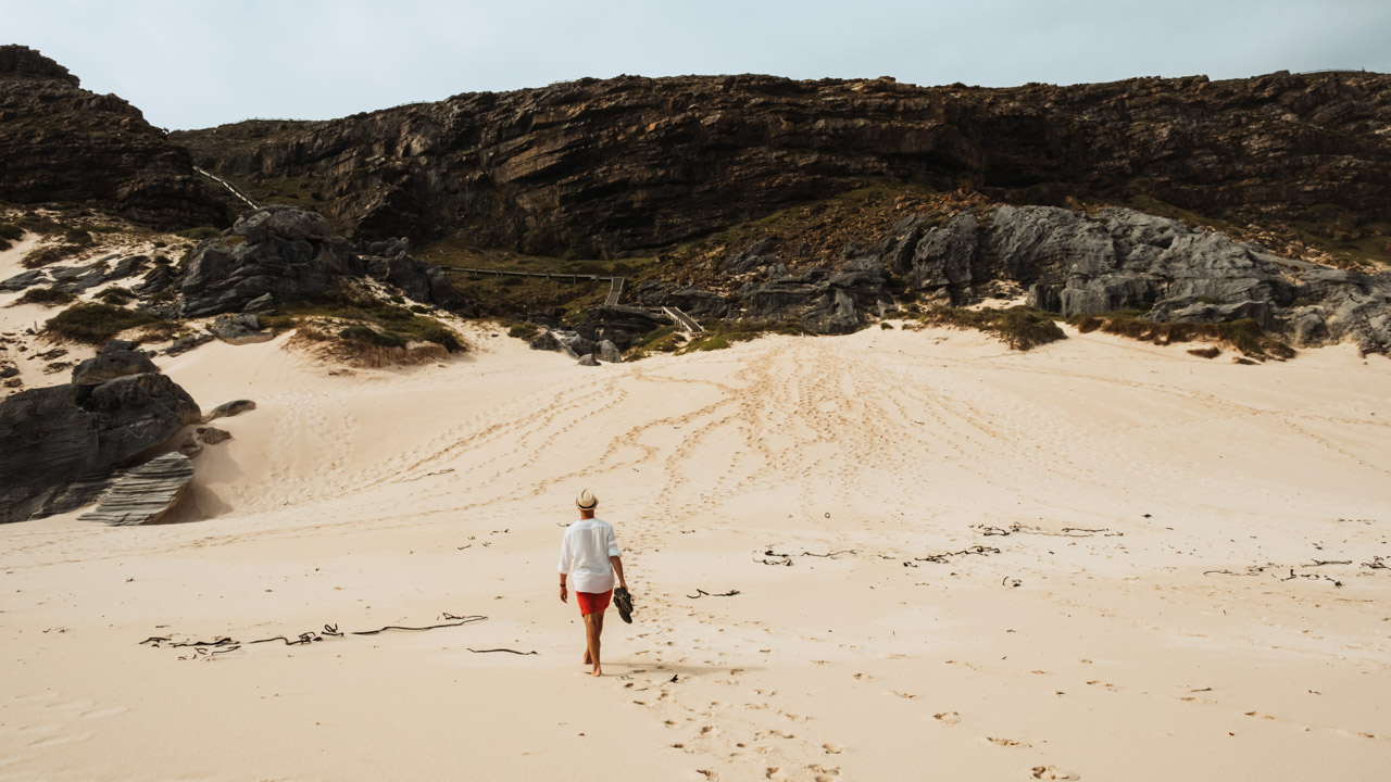 Godahoppsudden, en man går från kameran och stranden mot en stig i sanden.
