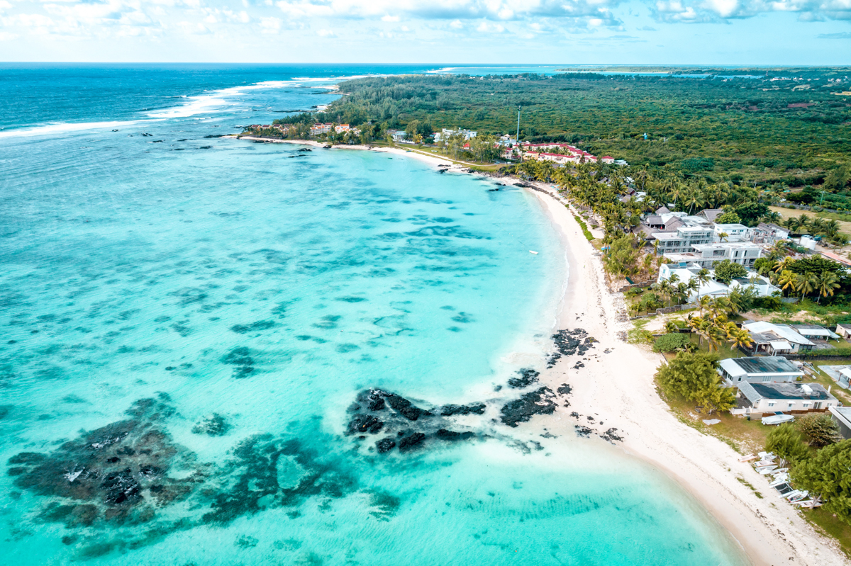 Belle Mare i Mauritius är perfekt för dig som söker ett lugnt strandliv. På bilden, som är fotograferad ovanifrån, ser du det turkosblå havet till vänster med den långa stranden till höger, och några resorts som ligger nära stranden. I bakgrunden en udde eller näs som är helt grön.